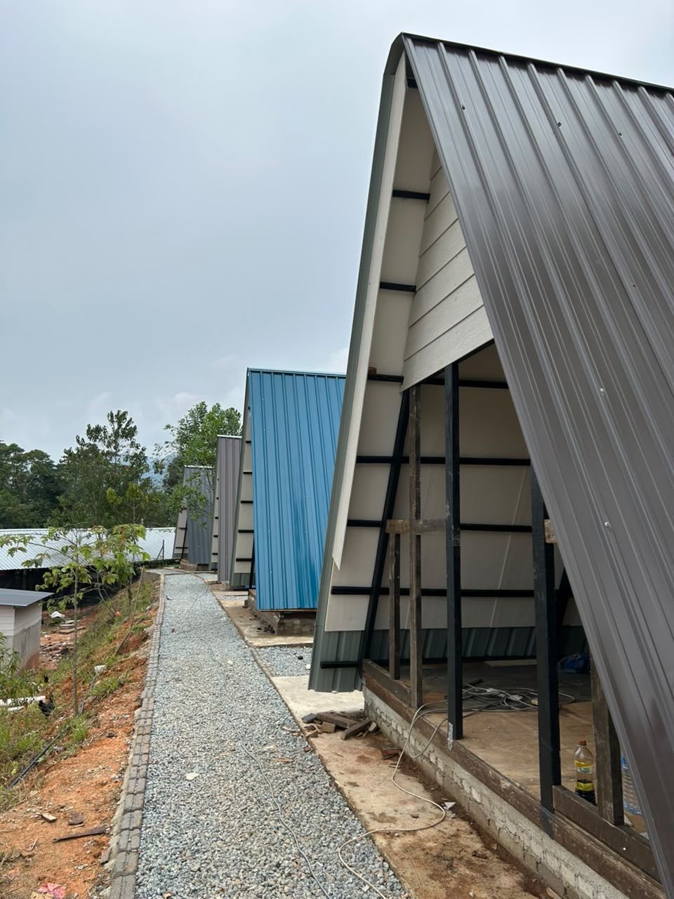 Deretan unit A-frame yang sedang disiapkan di sepanjang laluan kerikil, dengan sebuah A-frame biru di belakang
